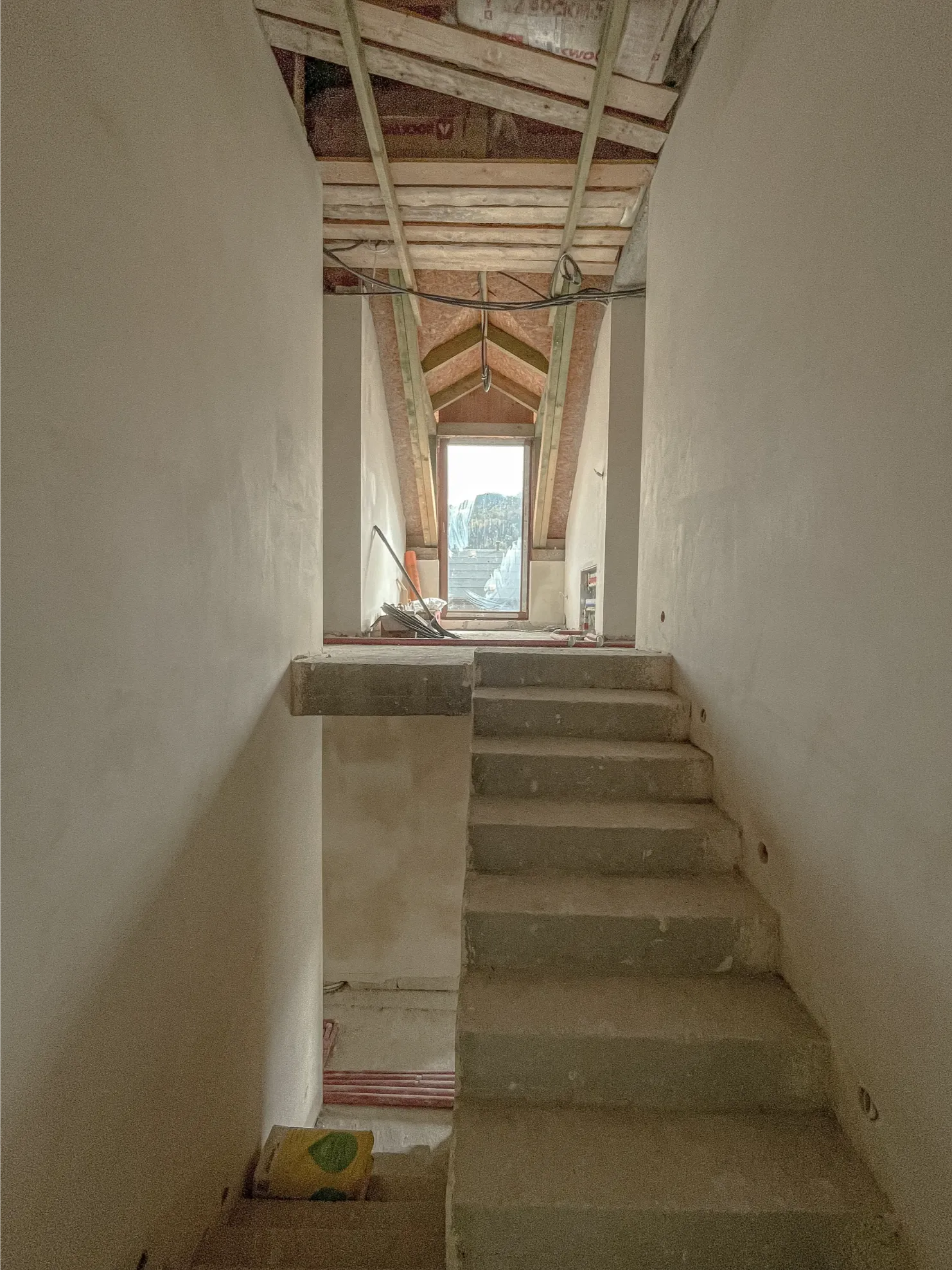 Betonowe schody i gładkie tynkowane ściany pod skosem dachu w trakcie zabudowy poddasza