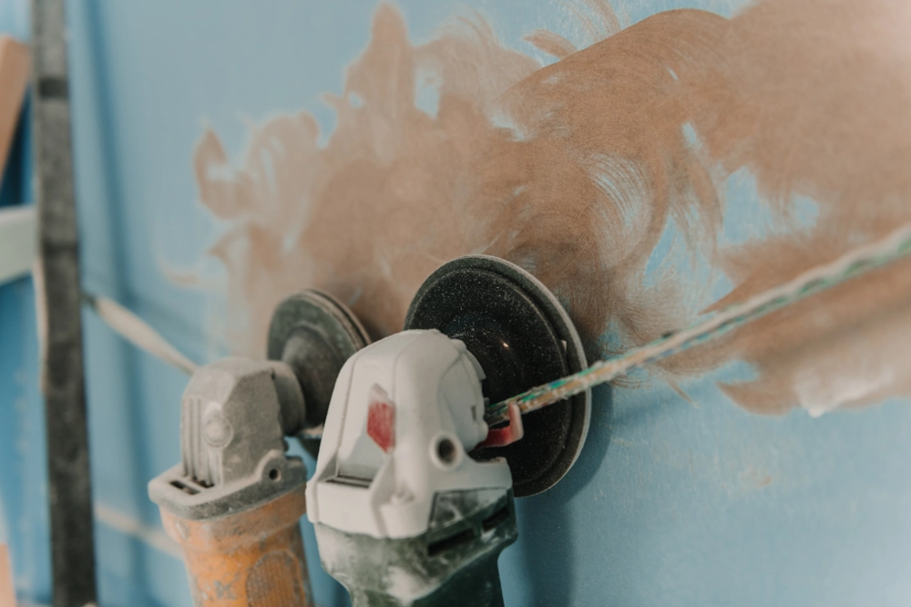 Elektryczna szlifierka z tarczą szlifierską podczas szlifowania gładzi na ścianie