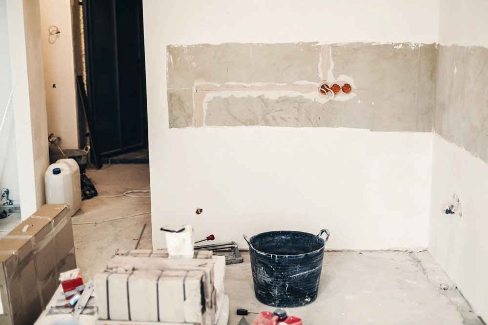 Wnętrze pomieszczenia z maszynowym tynkiem na ścianie – Tynki gipsowe, wiadro i bloczki w tle